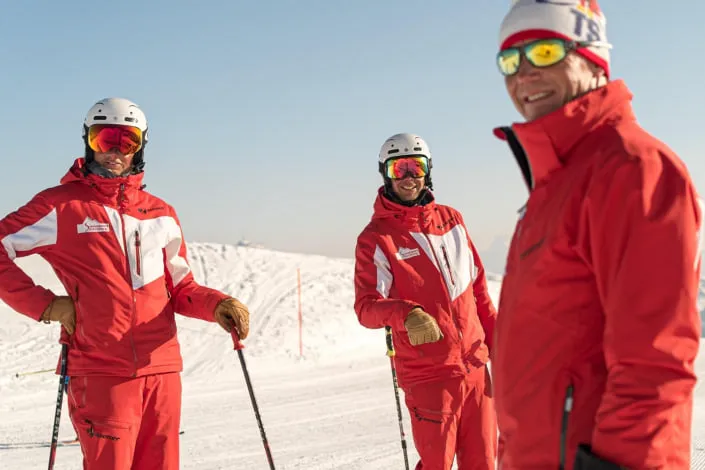 Three ski instructors in red outfits on the slopes