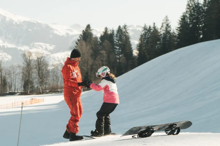 Instructor helps a child with snowboarding in Kirchberg
